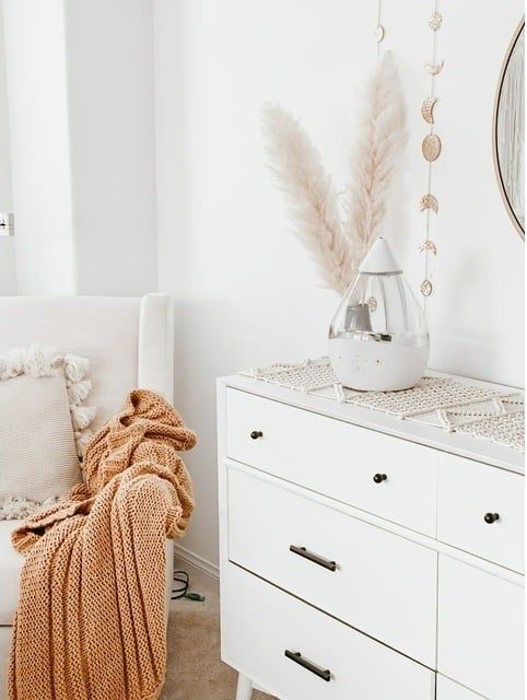 Cozy corner in a room with a white dresser, a knitted throw draped over it, and decorative accents on display