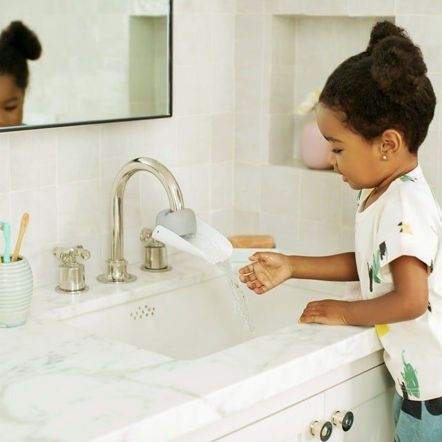 Child washing hands at the sink, reflected in the mirror, wearing a graphic tee