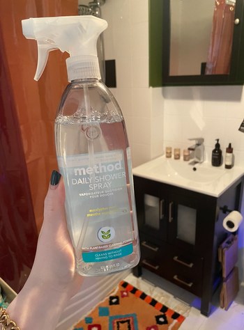 A person holding a Method Daily Shower Spray bottle in a bathroom setting