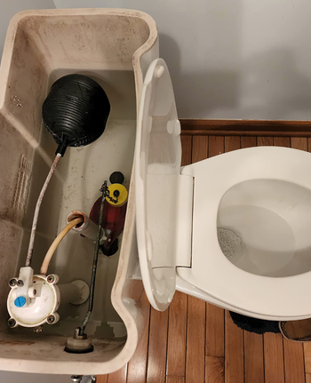 An open toilet tank displaying the internal parts connected to the flush mechanism. The image emphasizes the mechanics inside the tank
