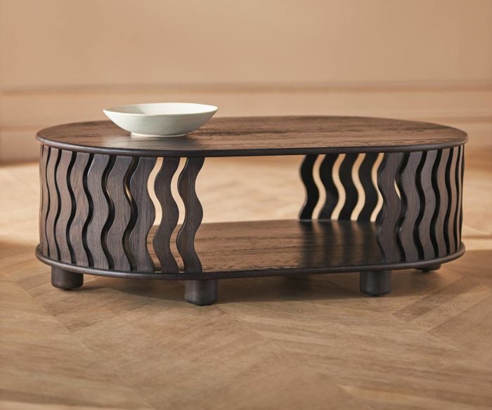 A wooden coffee table with a wavy, open design, topped with a white bowl, set in a minimalist styled room.