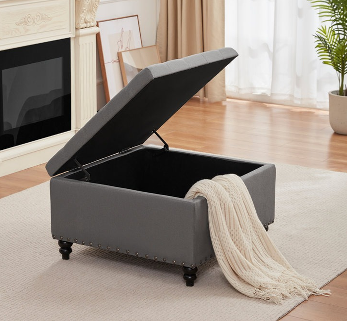 The ottoman in light gray with the top opened to reveal hidden storage inside.