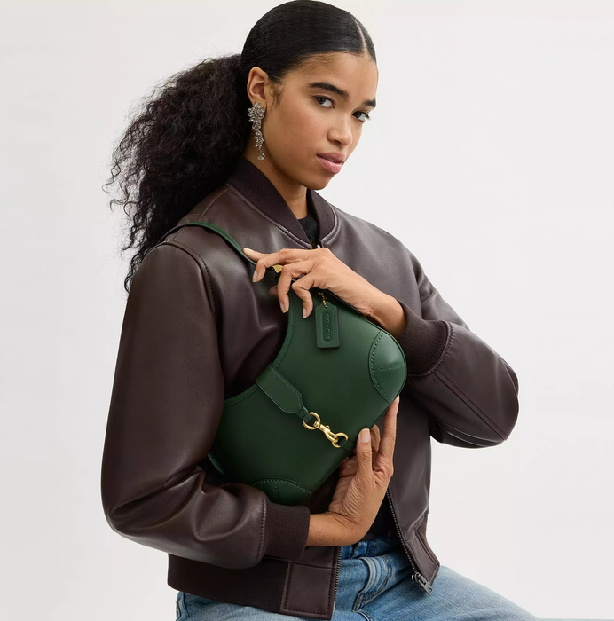 A person wearing a brown leather jacket, holding a trendy green handbag.