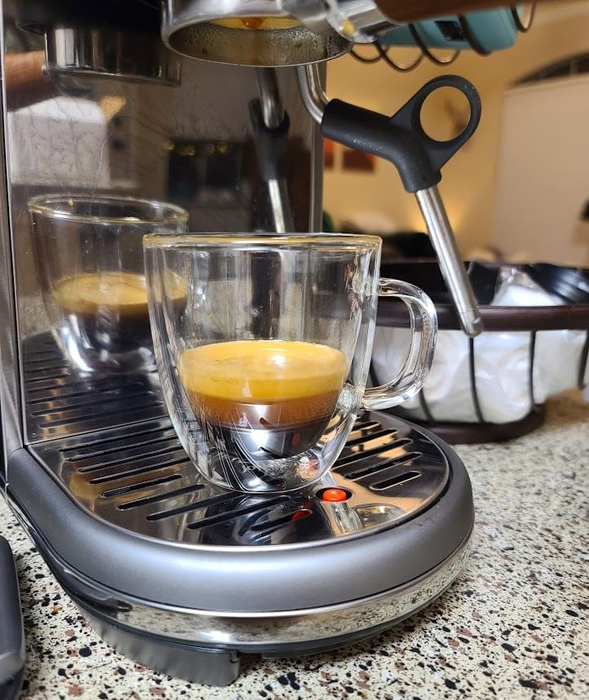 An espresso machine on a countertop with a freshly brewed shot of espresso in a glass cup, the steam wand positioned beside it.