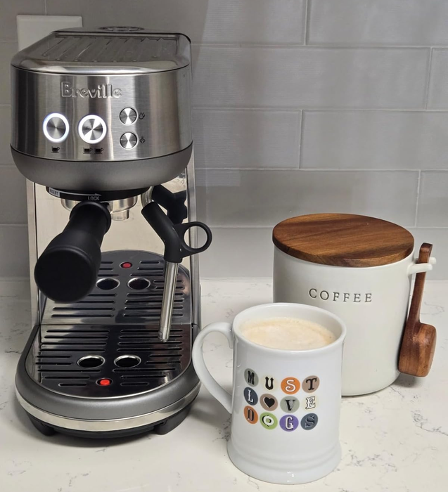 An espresso machine with a coffee canister and a mug that reads.
