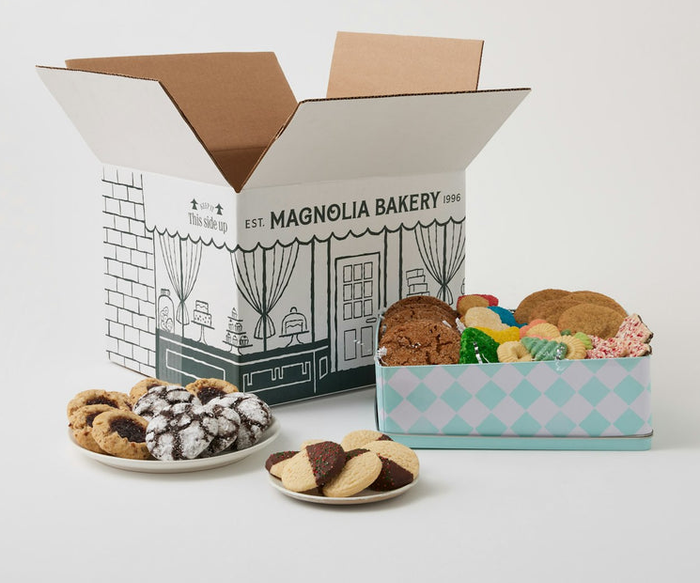 A Magnolia Bakery box open to reveal assorted cookies on a plate and in a checkered box, displayed for a shopping feature