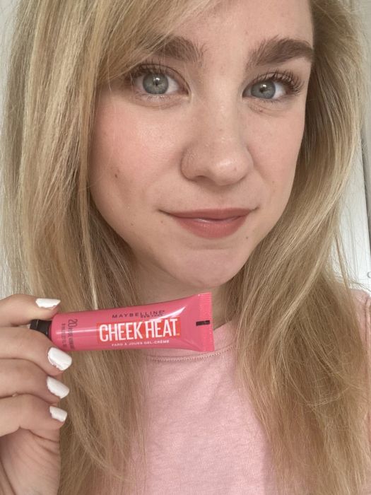 A Mytour editor holding a pink tube of Cheek Heat with the product applied to their cheeks.
