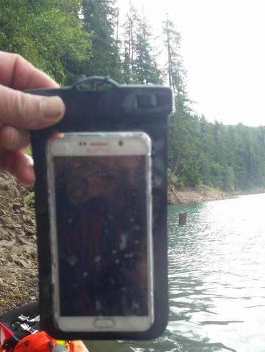 A reviewer holding their phone in the waterproof pouch, suspended above water.