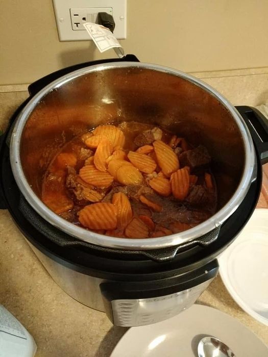 An electric pressure cooker placed open on a countertop, containing a cooked meal with sliced carrots and pieces of meat