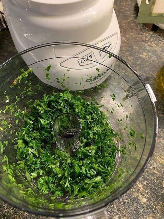A food processor filled with chopped parsley, the lid is removed, and the buttons display 