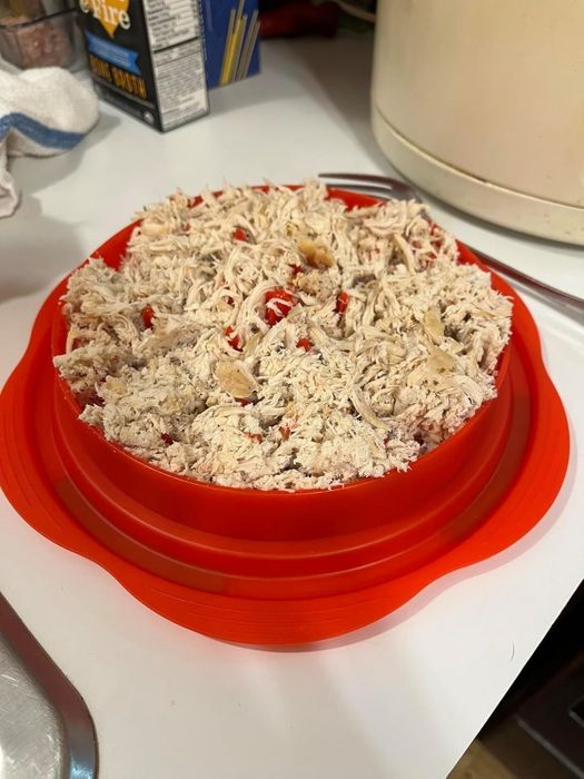 Shredded chicken placed in a red container on a kitchen counter, surrounded by various kitchen items and utensils