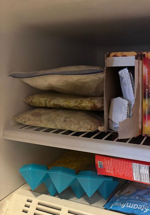 A freezer stocked with various items, including a pizza box and an ice tray, representing essential grocery items