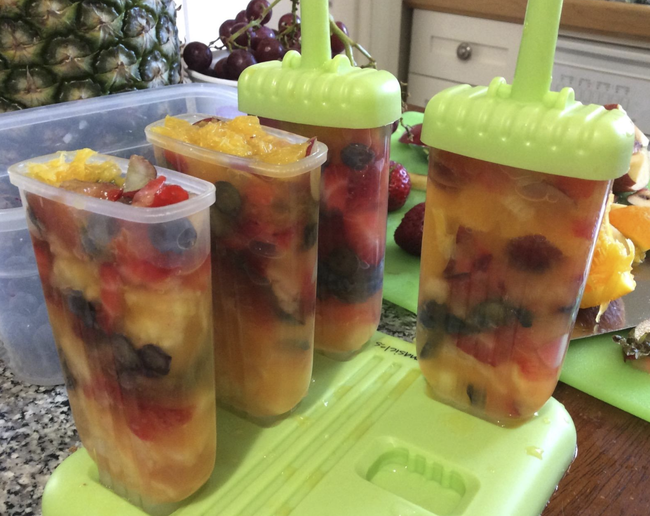Four popsicle molds filled with a fruit mixture. Two of them have the tops on, which will serve as the sticks.