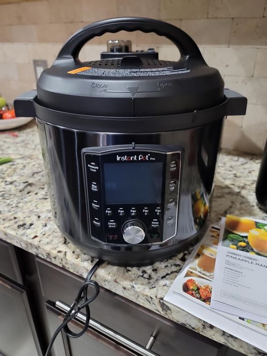 An Instant Pot Pro multi-cooker sitting on a kitchen countertop, plugged in and ready to use, with an open cookbook placed nearby