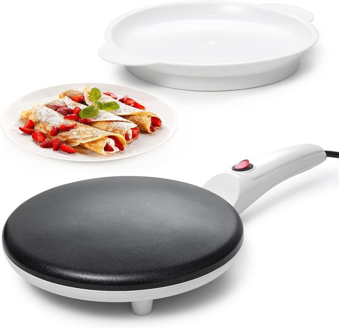 Electric crepe maker with its lid open, alongside a plate of crepes garnished with fresh strawberries and mint