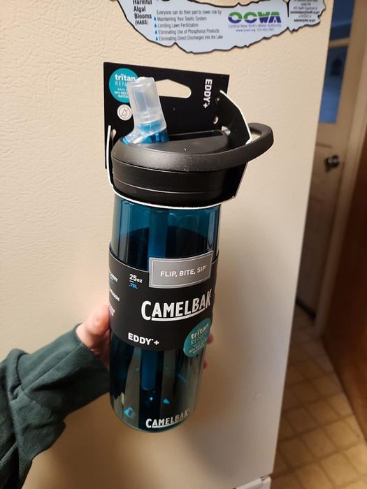 A hand holding a CamelBak Eddy+ bottle featuring a flip, bite, and sip nozzle