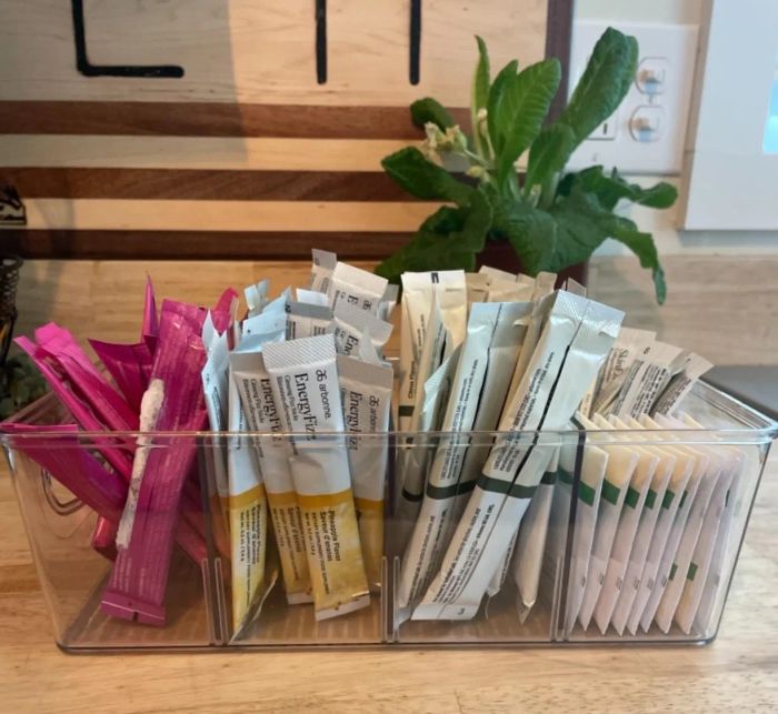 A transparent box filled with a mix of single-use condiment packets resting on a wooden countertop