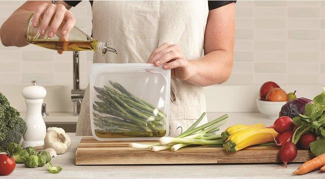 A person holding a Stasher bag with asparagus inside, pouring olive oil into the bag