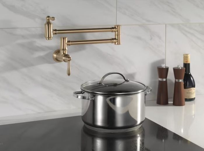 The gold faucet mounted on the wall above a glass cooktop with a large pot resting on it