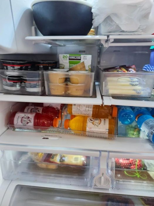 An open fridge stocked with various drinks like Gatorade and water, alongside food items such as Kirkland protein bars, yogurt, and cheese