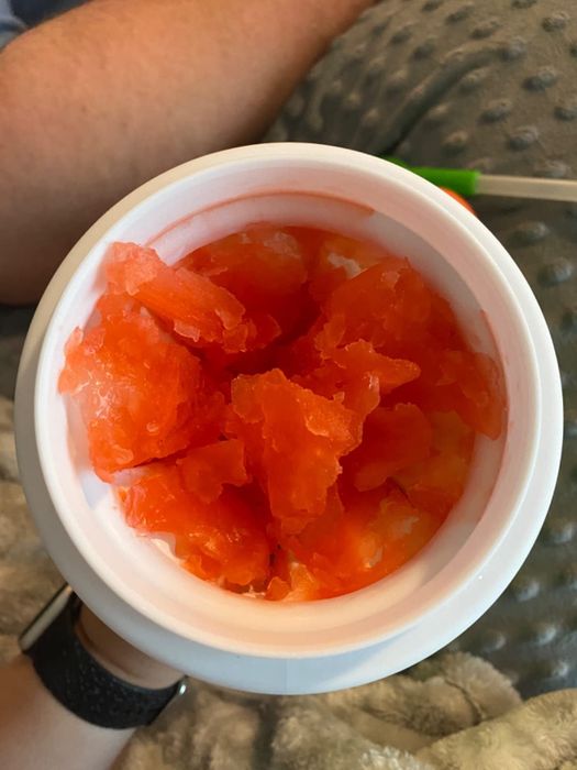 A hand is holding a cup filled with large, orange-colored chunks of crushed ice.