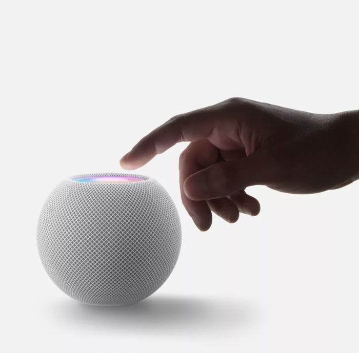 A hand poised to touch the vibrant top surface of the white Apple Homepod mini speaker.