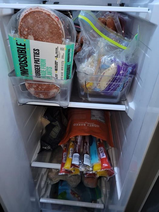 A freezer packed with Impossible burger patties, assorted frozen meats in bags, and various frozen snacks