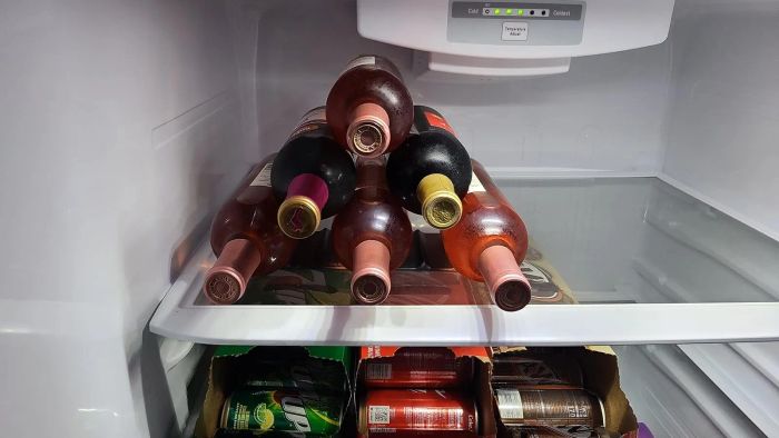 Wine bottles and cartons of drinks neatly arranged on shelves inside a refrigerator