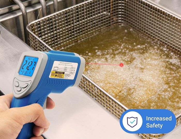 A hand uses a digital non-contact thermometer to measure oil temperature in an industrial fryer, with a text promoting safe measurements and improved safety.