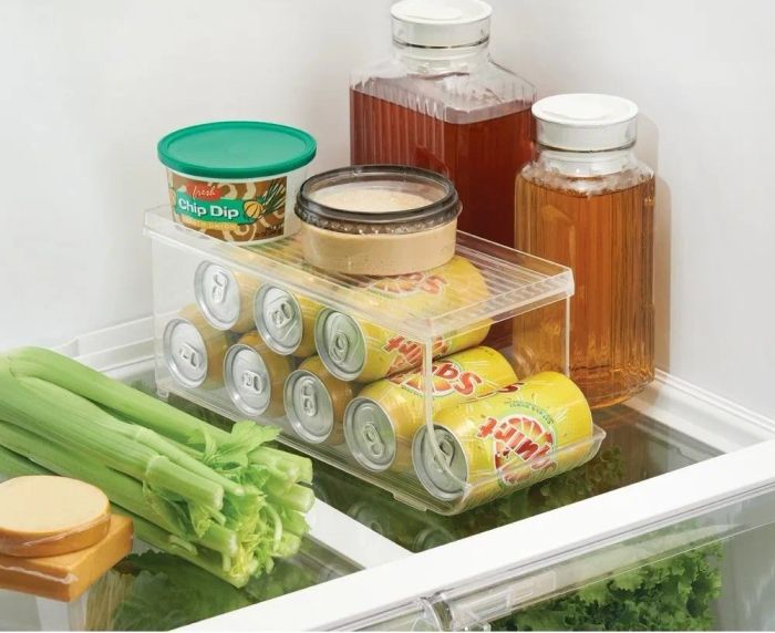 A fridge shelf with drink pitchers and a large soda can organizer, keeping cans arranged horizontally for easy access each time