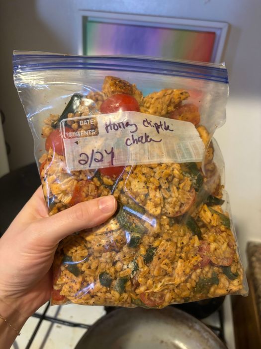 A hand holding a labeled freezer bag filled with homemade chipotle chicken