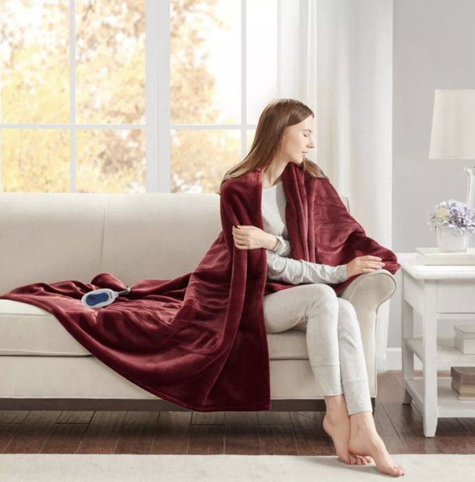 A model relaxing on a couch, with a red blanket wrapped around their shoulders