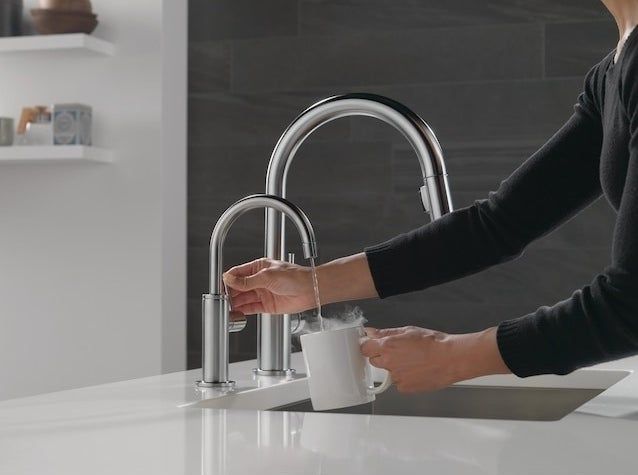 A person using the hot water faucet to fill up a mug