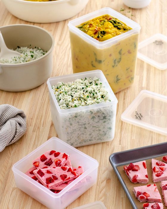 Containers holding frozen meals: curry, herb-infused rice, strawberries in freezer-friendly containers, and other frozen goodies on a wooden surface