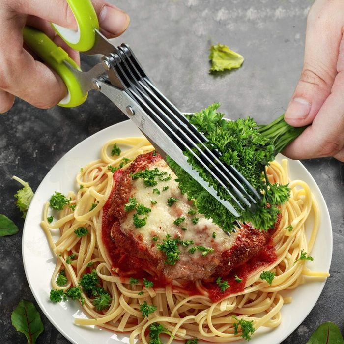 A pair of hands garnishing parsley on a plate of spaghetti and meatloaf