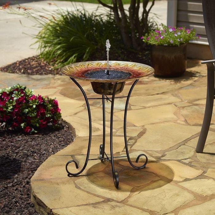 A beautifully designed sunflower pedestal birdbath, set on a patio, with water gently bubbling from the top.