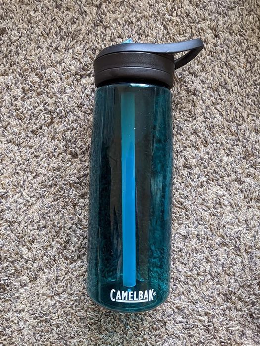 A CamelBak water bottle with a flip-top lid resting on a carpeted floor