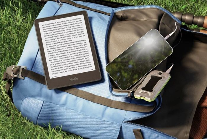 The black Kindle e-reader placed on a backpack resting on the grass.