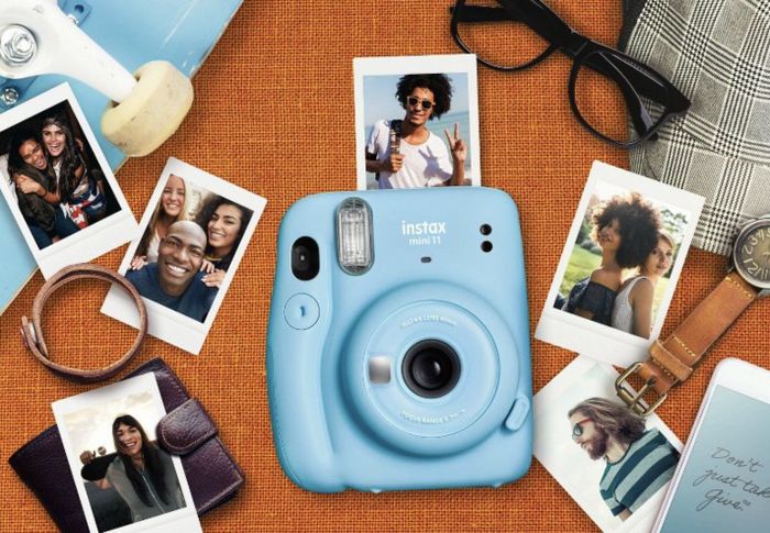A blue camera surrounded by Polaroid photos scattered across a desk