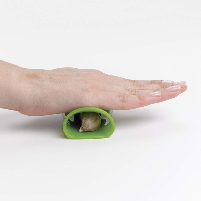 A hand rolling an unpeeled garlic clove inside a silicone sleeve