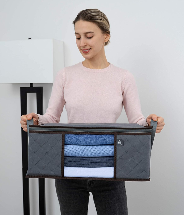 A person holds a fabric storage organizer filled with neatly folded clothes, standing in a minimalist room that highlights the storage solution's simplicity and efficiency.
