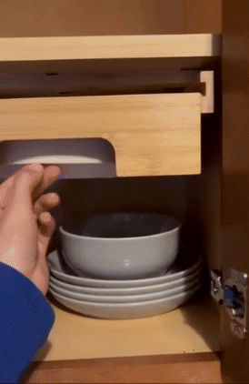 A person is pulling paper plates from a bamboo holder placed beneath a cabinet.
