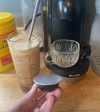 A hand holding a coffee pod with a sticker lid affixed to it.