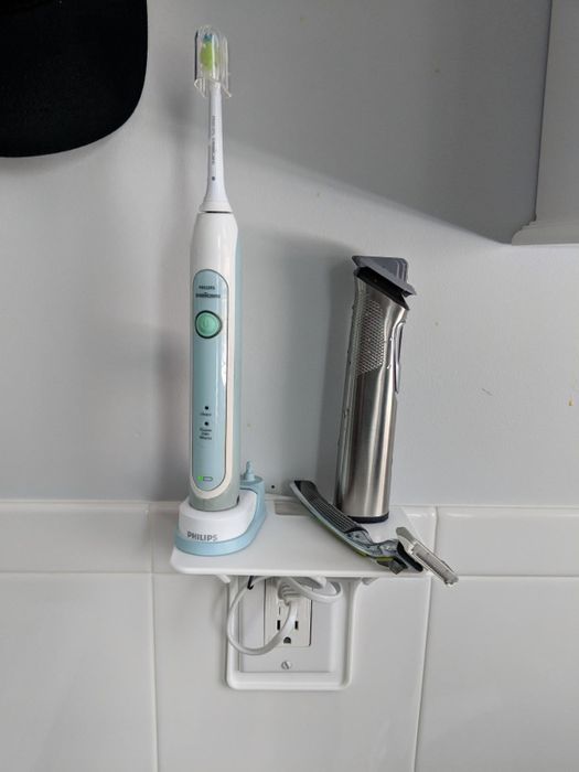 A reviewer's photo showing the outlet shelf being used to store a toothbrush and razor.