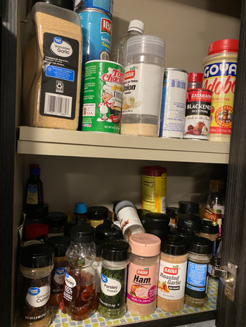 A reviewer’s photo showing a cluttered kitchen cabinet filled with spice jars