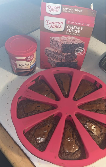 A photo showing freshly baked brownies in a slice-shaped silicone pan alongside Duncan Hines brownie mix and Rich & Creamy frosting