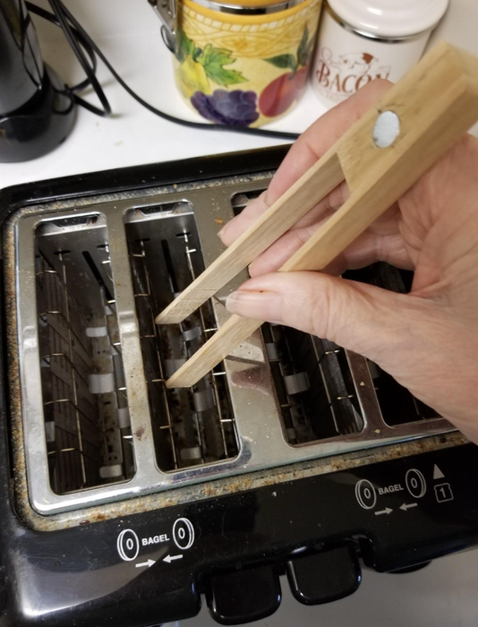 A person using a wooden tool to retrieve something from a toaster