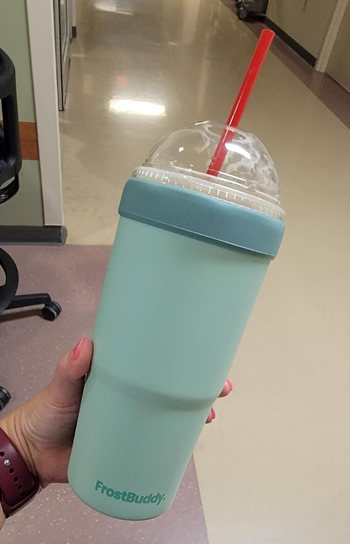 A person holding a blue FrostBuddy insulated tumbler with a Dunkin' cup placed inside.
