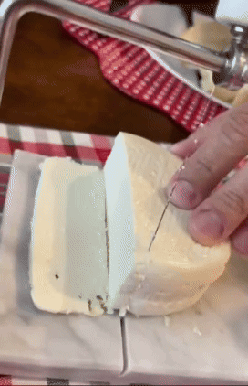 Reviewer using a white marble cheese slicer to cut through soft cheese with a wire