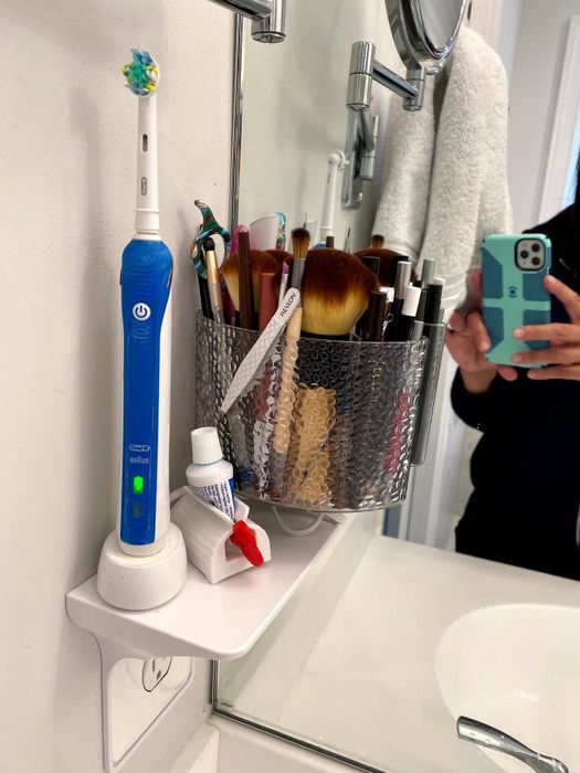 A reviewer's photo showing the outlet shelf holding makeup brushes, a toothbrush, and other items.